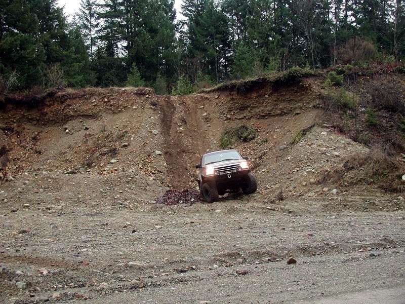 Lifted SUV driving up a steep, rocky hill in a wooded area.