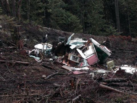 1985 Ford Bronco - A destroyed trailer home and debris are scattered across a wooded hillside.