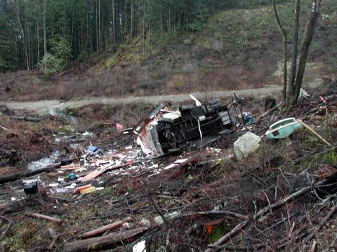 1985 Ford Bronco - A heavily damaged RV or camper trailer has overturned and is strewn across a debris-filled wooded hillside. The wreckage is scattered among…