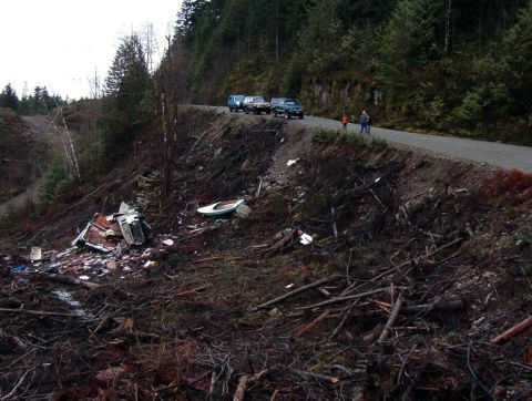 1985 Ford Bronco - A scene of a hillside covered in debris, including broken structures and a small boat, next to a road where several vehicles are parked.