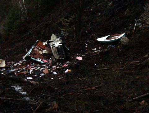 1985 Ford Bronco - A wrecked vehicle, possibly a camper or RV, is overturned and debris is scattered across a wooded hillside. A small white boat rests on the…