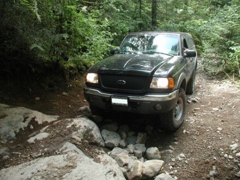 1985 Ford Bronco - A black Ford Ranger pickup truck navigates a rocky, wooded trail.