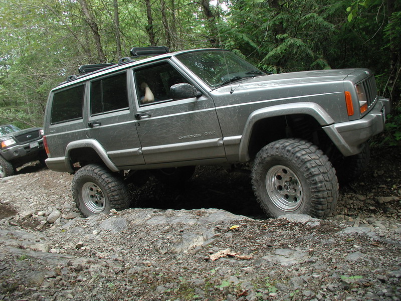 Gray Jeep Cherokee XJ off-roading over rocks, front tire lifted.