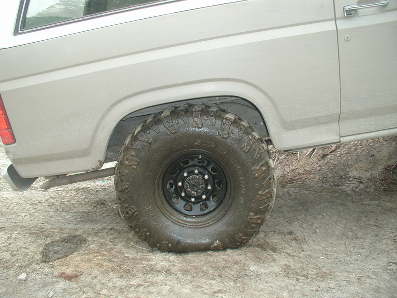 Rear passenger side of a light-colored Ford Bronco with a muddy off-road tire.
