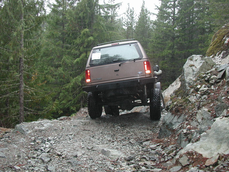Brown SUV off-roading on a rocky trail in a forest.