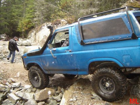 1985 Ford Bronco - A blue Ford Bronco is navigating a rocky, off-road trail with a snorkel installed. A person in a black jacket walks behind the vehicle on t…