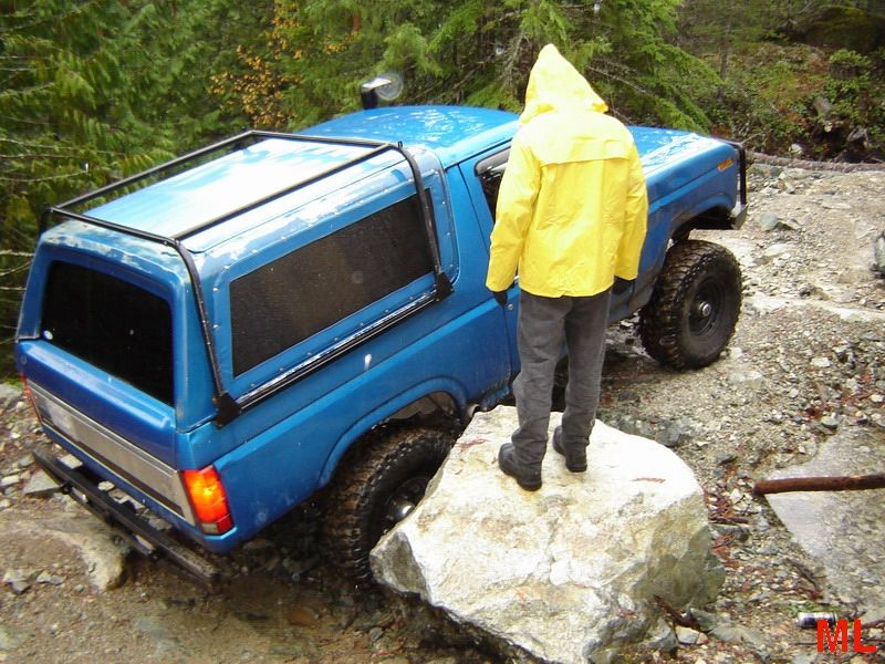 Blue Ford Bronco on a rocky trail with a person in a yellow raincoat.