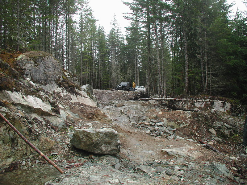 Two SUVs parked on a rocky trail in a forest.