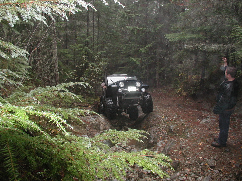 Black Jeep Wrangler driving on a rocky, wooded trail.