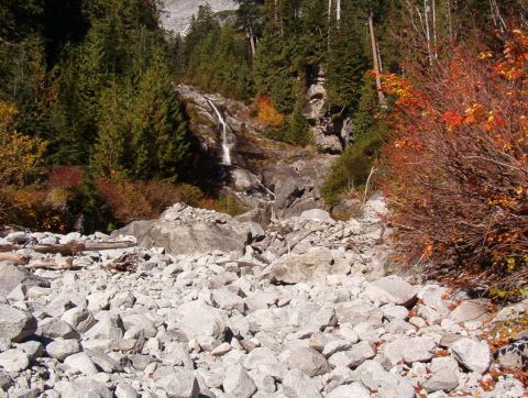 1985 Ford Bronco - A rocky streambed leads up to a waterfall cascading down a rocky slope, surrounded by evergreen trees and autumn foliage.