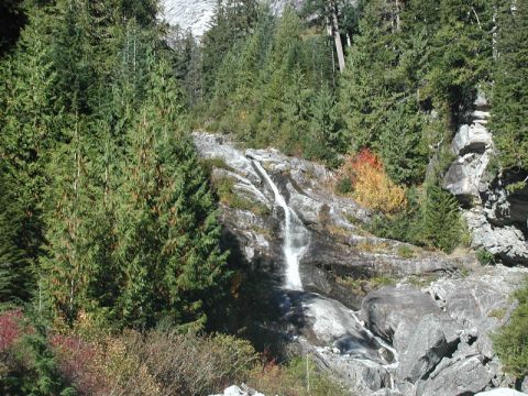 1985 Ford Bronco - A waterfall cascades down a rocky slope surrounded by evergreen trees and some autumn foliage.