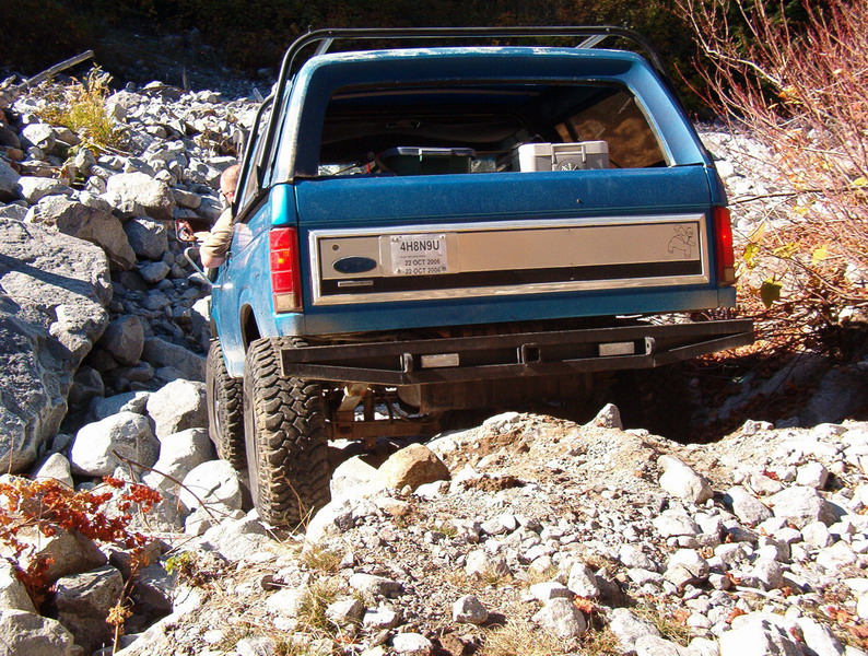 Teal Ford Bronco driving on a rocky off-road trail, rear view.