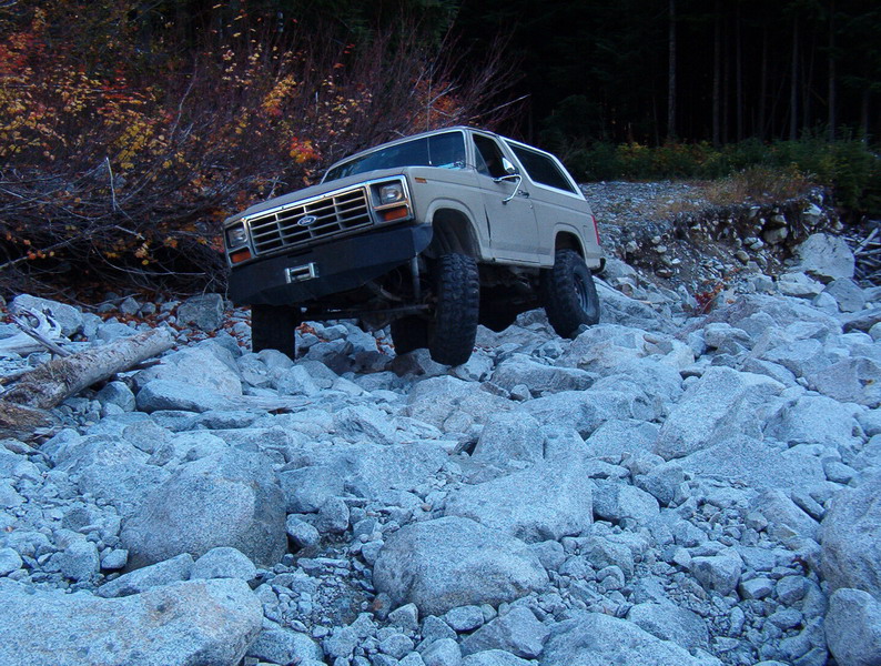 Tan 1980s Ford Bronco with off-road tires and winch bumper on rocky terrain.