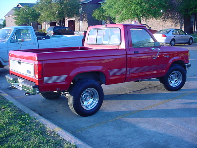 Red early-1990s Ford Ranger regular cab pickup, rear three-quarter view in a parking lot