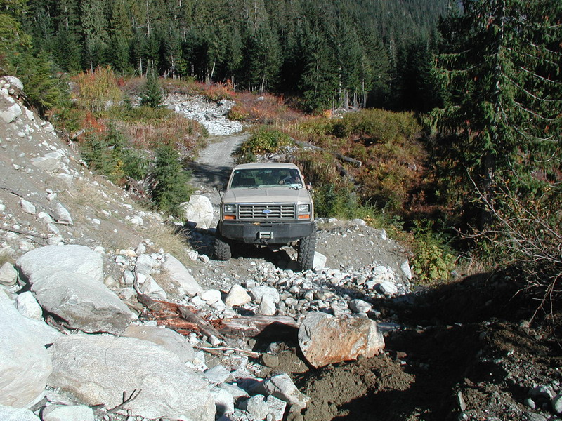 Tan 1980s Ford Bronco on a rocky forest trail.