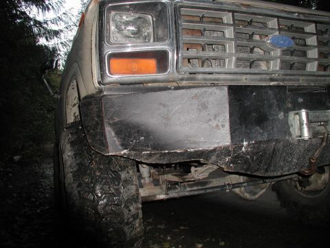 1985 Ford Bronco - Front quarter view of a white Ford Bronco with a custom black metal bumper and off-road tires. The vehicle is parked on a dirt road surroun…
