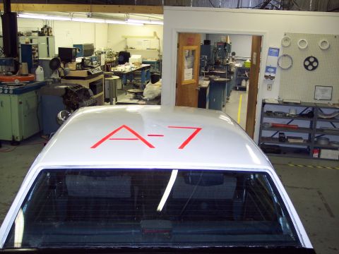 2001 Ford Crown Victoria - A white vehicle with red markings 'A-7' on its roof is parked inside a workshop.