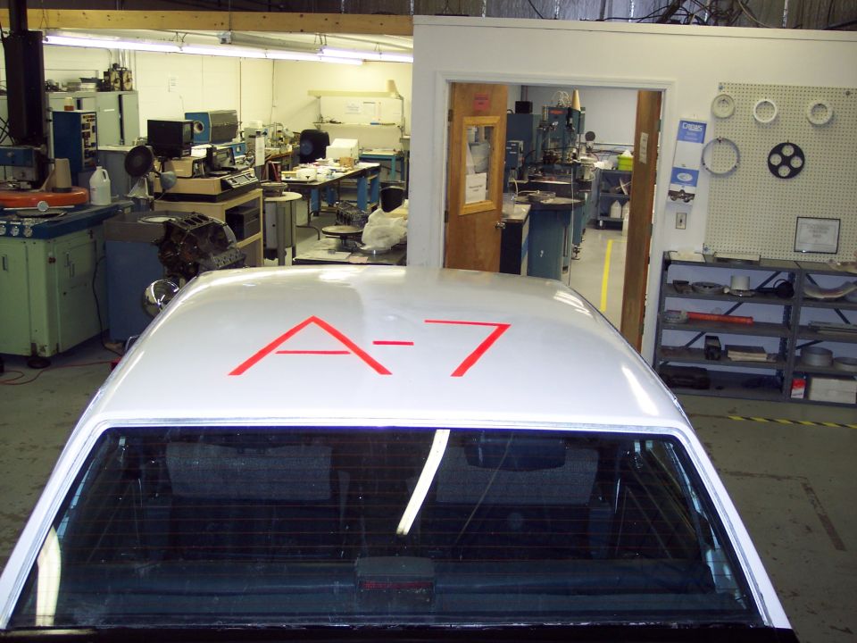 White car roof with red A-7 markings. Interior visible through rear window. Garage or workshop setting