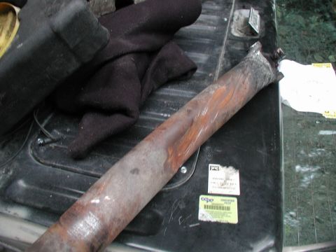 1985 Ford Bronco - A bent and rusted exhaust pipe lies on the black bed of a pickup truck, next to a black fabric item and some stickers. The exhaust pipe app…