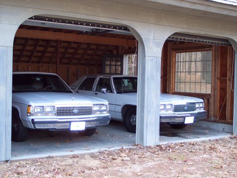 2001 Ford Crown Victoria - Two white 2001 Ford Crown Victorias are parked in a garage, viewed from the front.