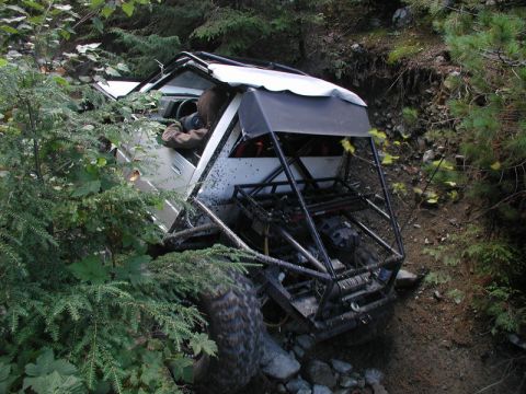 1985 Ford Bronco - A heavily modified off-road vehicle, likely a custom buggy or heavily altered Jeep, is tilted precariously on a steep, rocky embankment. Th…