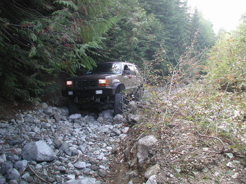 Brown SUV driving on a rocky, wooded trail.