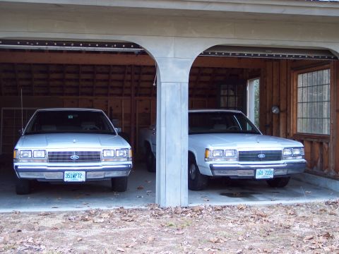 2001 Ford Crown Victoria - Two Ford Crown Victorias are parked side-by-side in a garage.