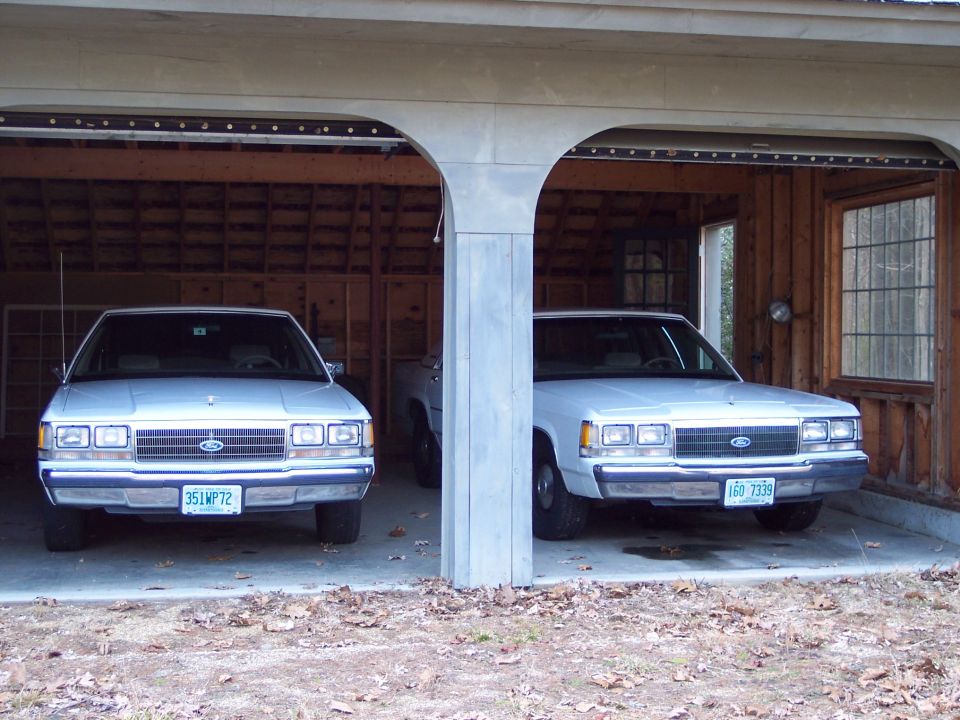 Two white Ford Crown Victorias parked in a garage. The one on the left has license plate 351WP72