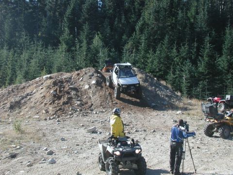 1985 Ford Bronco - A silver Toyota 4Runner is climbing a dirt hill, with several ATVs and people gathered below. A person is filming the action with a video c…