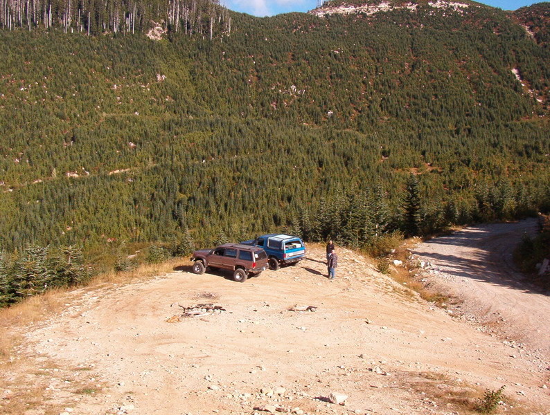 Two SUVs and a van parked on a dirt road with a mountain forest background.
