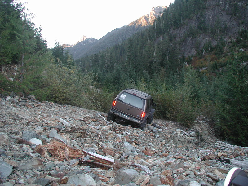 Brown SUV on a steep, rocky mountain trail with trees.