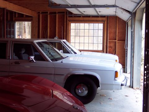 2001 Ford Crown Victoria - Two white sedans are parked in a garage, with a red car partially visible in the foreground.
