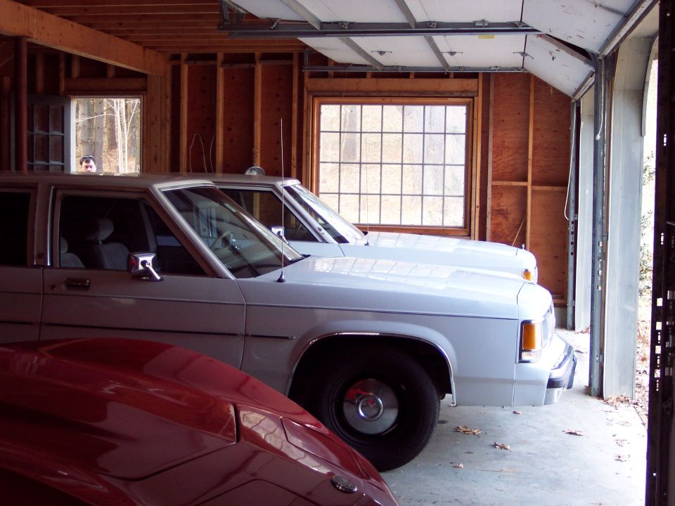 Two white sedans parked side-by-side in a garage. A red car hood is in the foreground
