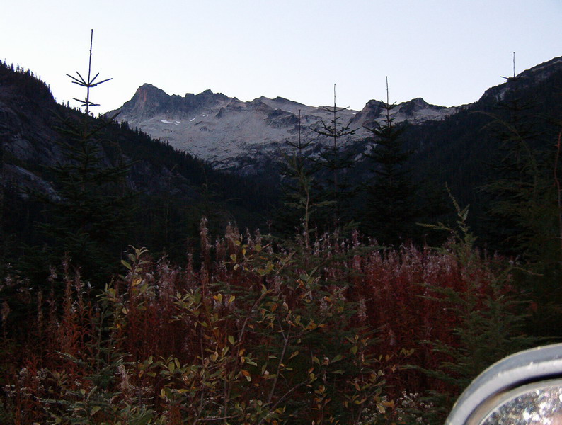 Mountain landscape at dusk with evergreen trees and rocky peak.