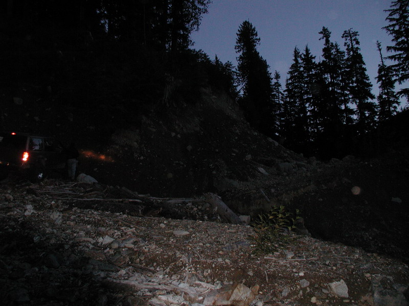 Dark SUV on a rocky trail at dusk, taillights on.