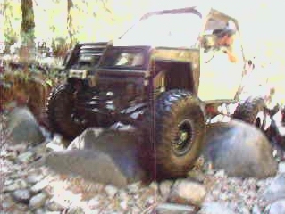 1985 Ford Bronco - A modified off-road vehicle with large tires navigates a rocky terrain. The front of the vehicle features a heavy-duty bumper and grille gu…