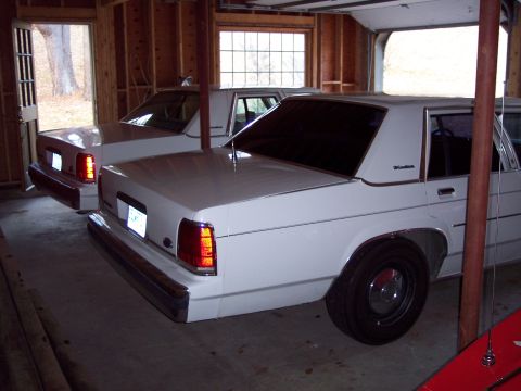 2001 Ford Crown Victoria - Two white sedans are parked inside a garage with the door open to the outside.