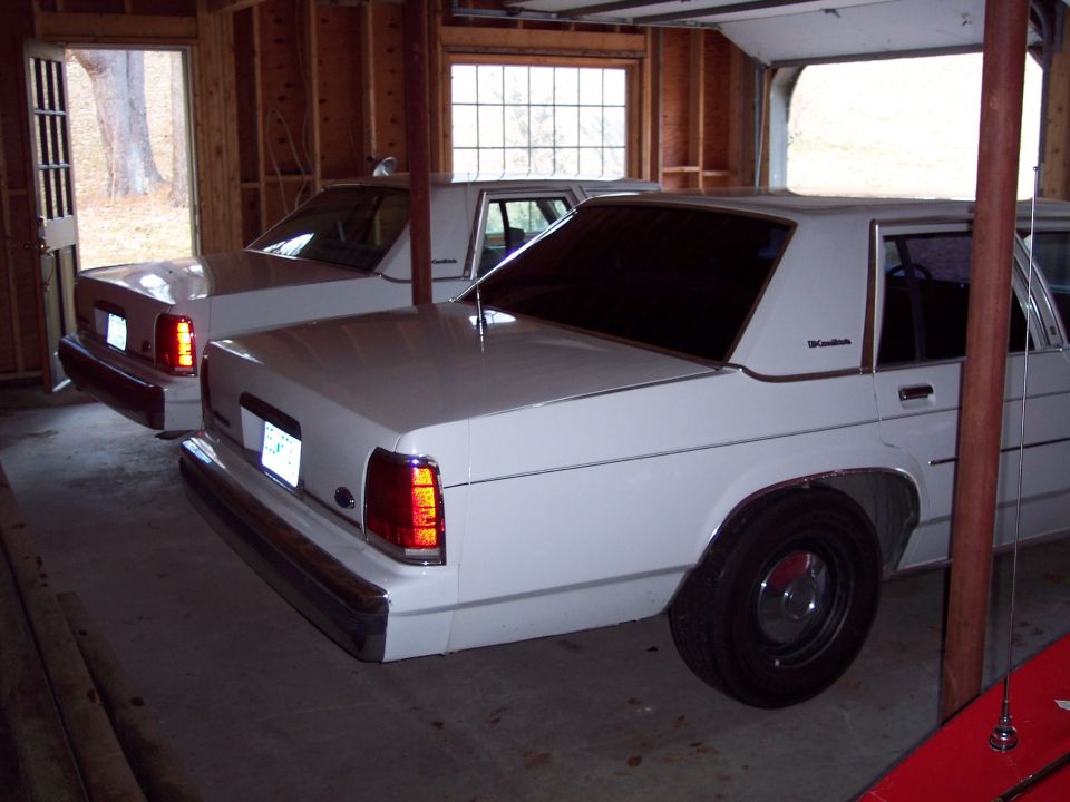 Two white sedans parked in a garage, one in the foreground showing its rear quarter panel and taillight