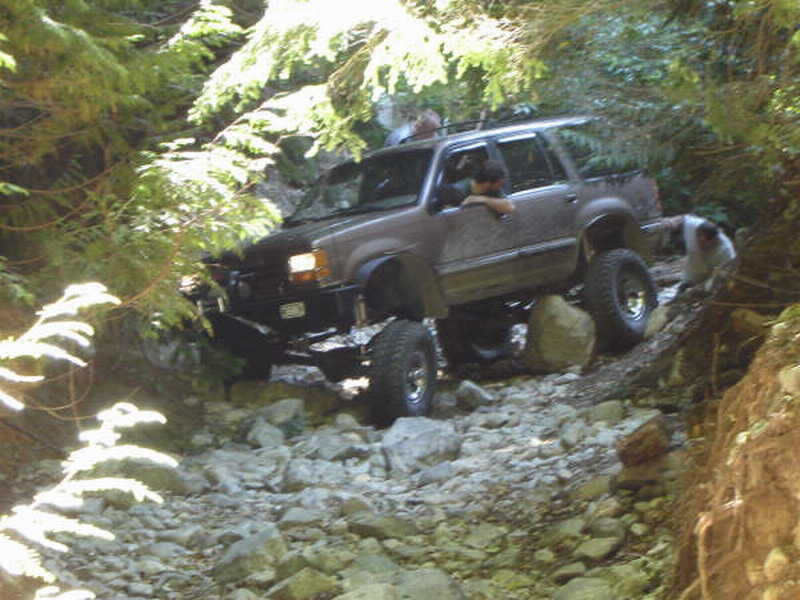 Lifted dark SUV driving over rocks on a wooded trail.