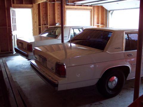 2001 Ford Crown Victoria - Two sedans are parked side-by-side in a garage with unfinished wood paneling.