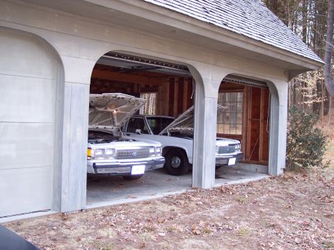 2001 Ford Crown Victoria - Two white Ford Crown Victorias are parked in a garage with their hoods up.