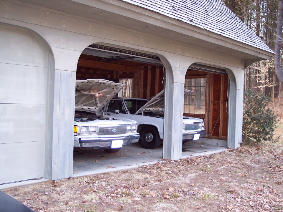 Two white Ford Crown Victorias with hoods open in a garage