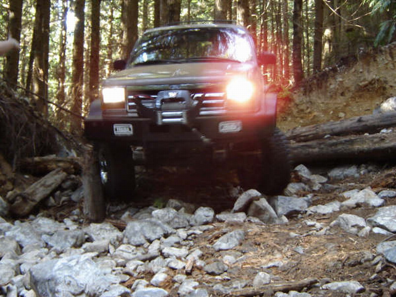 1985 Ford Bronco on a rocky forest trail, front view.