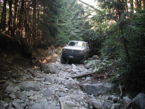 Lifted 1980s Ford Bronco on a rocky, wooded trail.