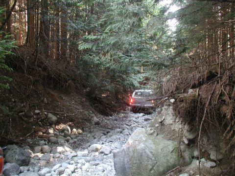 White pickup truck driving on a rocky, wooded trail.