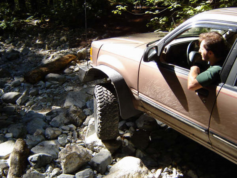 Tan SUV driving off-road over rocks with a man driving.