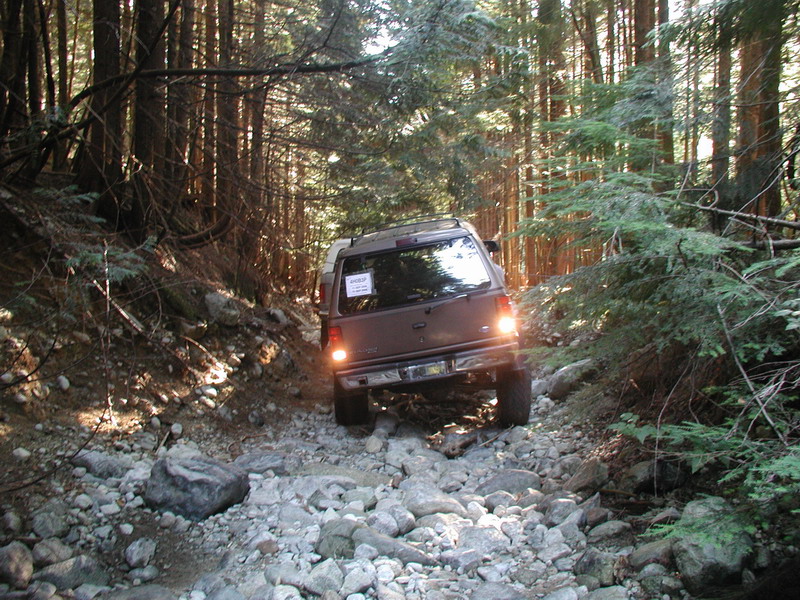 Dark SUV off-roading on a rocky, wooded trail.