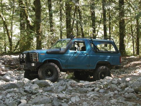 Blue Ford Bronco on a rocky forest trail with off-road tires and snorkel.