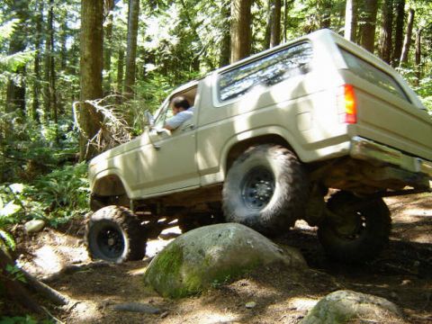 Tan Ford Bronco off-roading on a rocky, wooded trail.
