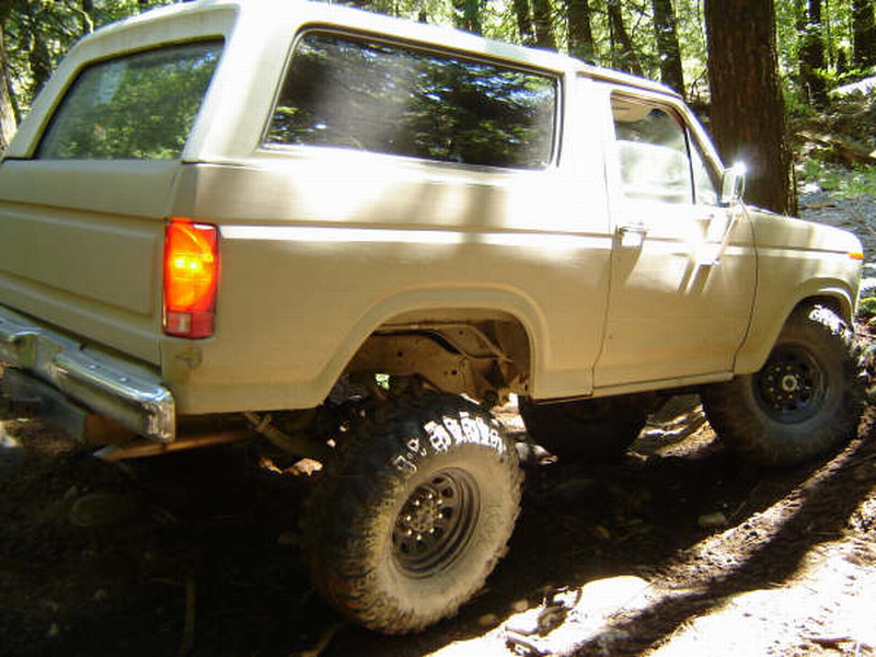 Tan Ford Bronco with off-road tires on a dirt trail.